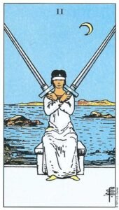 Carta del Dos de Espadas del Tarot Rider Waite: una mujer con los ojos vendados y túnica blanca cruzando dos espadas frente al mar.