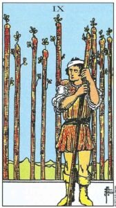 Carta del Nueve de Bastos del Tarot Rider Waite: un hombre herido con un vendaje en la cabeza, apoyado en un bastón mientras otros ocho forman una barrera tras él.