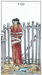 Carta del Ocho de Espadas del Tarot Rider Waite: una mujer con los ojos vendados y atada, rodeada por ocho espadas clavadas en el suelo embarrado.