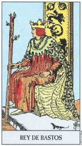 Carta del Rey de Bastos del Tarot Rider Waite: un rey sentado de perfil en un trono decorado con leones y salamandras, sosteniendo un gran bastón florecido.