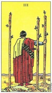 Carta del Tres de Bastos del Tarot Rider Waite: un hombre de espaldas mirando barcos en el mar desde una colina, apoyado en uno de sus tres bastones.